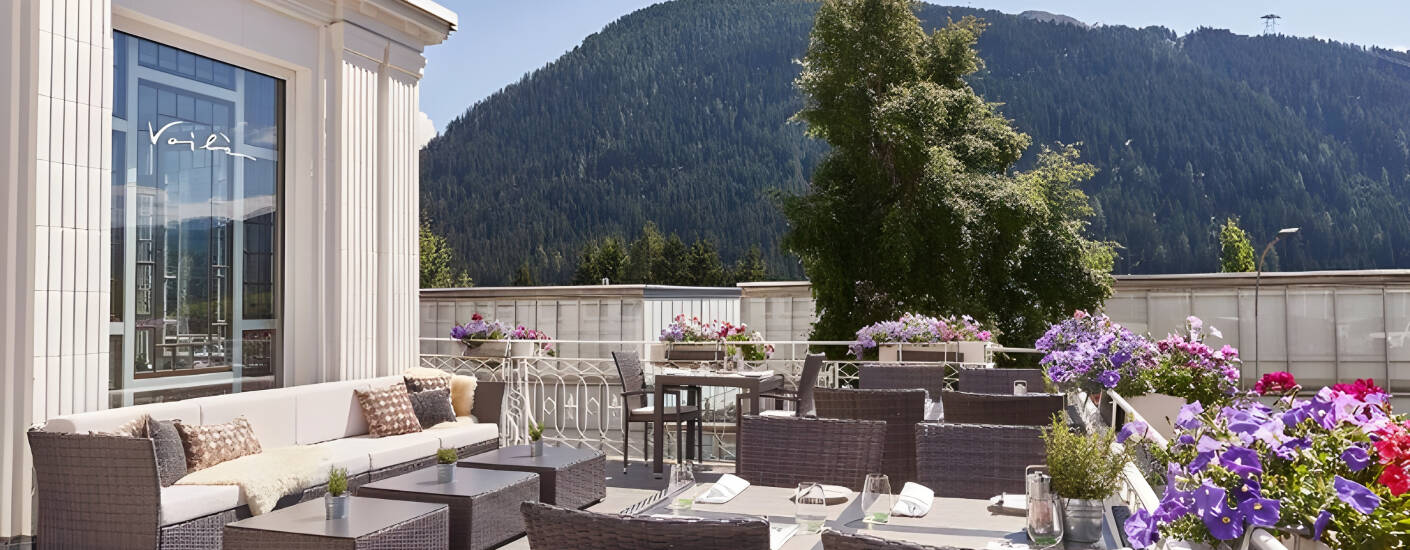 Ta plass på hotellets innbydende solterrasse og nyt en forfriskning med flott utsikt over fjellene rundt Davos.