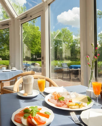 Beginnen Sie Ihren Tag mit einem reichhaltigen Frühstücksbuffet und genießen Sie den Blick auf den Garten vom Frühstücksraum des Hotels.