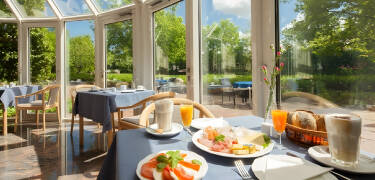Beginnen Sie Ihren Tag mit einem reichhaltigen Frühstücksbuffet und genießen Sie den Blick auf den Garten vom Frühstücksraum des Hotels.